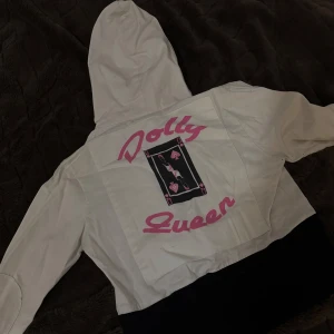 Söt jacka  - Söt jacka med tryck på baksidan som står Dolly Queen med huva och dragkedja framtill. Jackan har två dragkedjefickor på bröstet och en unik design med text och kortmotiv på ryggen. Passar S & M