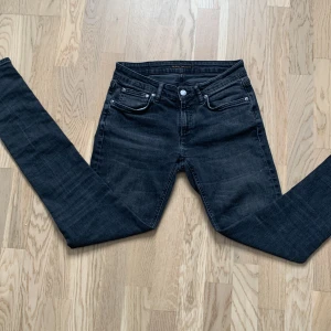 Svarta jeans från Nudie Jeans - Ett par Snygga svarta jeans i storlek W28 L34 från Nudie Jeans med klassisk femficksdesign och knappgylf. Jeansen har en stilren look med diskreta sömmar och en bekväm passform. Perfekta för en avslappnad stil.  