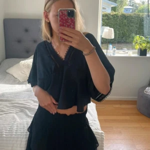 Svart axelbandslös topp/kjol - Kjol med volangdetaljer. Perfekt för varma sommardagar eller en kväll ute. Den har en luftig passform och är tillverkad i ett lätt material som ger en skön känsla. Kan även användas som topp