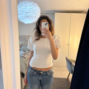 Vit topp med puffärmar från H&M - Säljer en söt vit topp från H&M med puffiga kortärmar. Toppen har en rund halsringning och är gjord i ett mjukt bomullsmaterial. Perfekt för en stilren look! 🌟