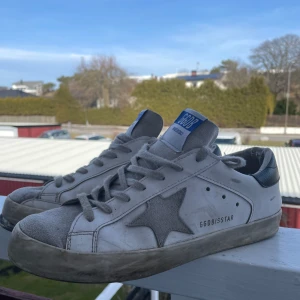  Golden Goose - Snygga vita sneakers från Golden Goose med en grå stjärndetalj på sidan. Skorna är i ganska så dåligt skick, säljer då ja behöver bli av me de så snabbt som möjligt. Stort hål vid tån på högra skon, går att fixa med rätt material.