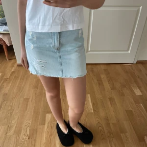 Ljusblå jeanskjol - Säljer en snygg ljusblå jeanskjol med slitna detaljer och rå kant. Kjolen har en klassisk femficksdesign och en bekväm passform. Perfekt för en avslappnad stil. Passar bra till en enkel t-shirt eller en trendig topp.
