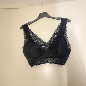 Svart spets bralette - Säljer en elegant svart spets bralette med v-ringad design. Den har breda axelband och ett vackert spetsmönster som ger en romantisk känsla. Perfekt för att bära under en blus eller som den är.