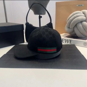 Svart keps med mönster och ränder - Snygg svart keps med diskret mönster och ikoniska ränder i grönt och rött på sidan. Perfekt för att ge din outfit en stilren touch.