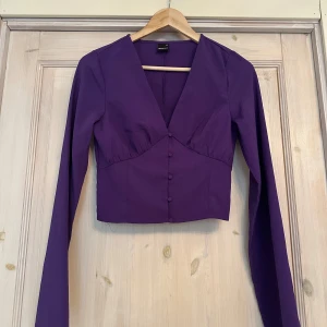 Lila blus från Gina Tricot - Snygg lila blus från Gina Tricot med långa vida ärmar och knappar framtill. Perfekt för en stilren look. Storlek XS.