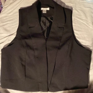 Svart väst från New Yorker - Snygg svart väst från Amisu i en klassisk design. Västen har en stilren look med en v-ringad framdel och är perfekt för att komplettera din outfit.