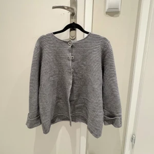 Grå kofta från Giolli - Säljer en stilren grå kofta från Giolli. Den har rund halsringning och knappar framtill. Koftan är ribbad och har långa ärmar med uppvikta muddar. 