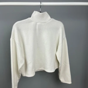 Vit polotröja från Zara - Säljer en stilren vit polotröja från Zara. Tröjan är croppad med långa ärmar och har en ribbad polokrage som ger en trendig look. Perfekt för kyligare dagar.
