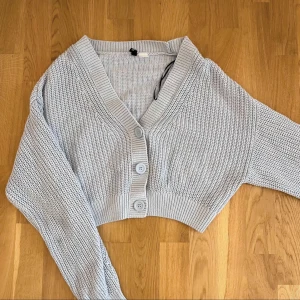 Ljusblå stickad kofta från H&M Divided - Säljer en ljusblå stickad kofta från H&M Divided. Koftan har en v-ringad design med knappar framtill och långa ärmar. Perfekt för en avslappnad stil. Passar bra till både jeans och kjol.