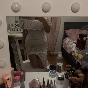 Vit spetsklänning - Säljer en elegant vit spetsklänning med offshoulder-design och volangdetaljer. Klänningen är tight och kort, perfekt för speciella tillfällen. Den har en dragkedja i ryggen för enkel påklädning. Använd några gånger fast nytt skick