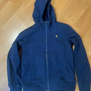 Mörkblå jacka med huva från Lyle & Scott - Säljer en mörkblå vårjacka från Lyle & Scott med huva och dragkedja i storlek 10-11 år. (Ca 140) 