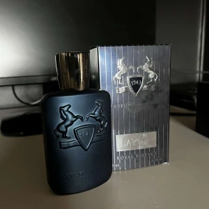 Parfym Layton  - Elegant parfymflaska i mörkblått med silverdetaljer från Parfums de Marly. Flaskan har en stilren design med en emblem av två hästar. Doften är en del av Royal Essence-kollektionen och kommer i en lyxig förpackning. Kvitto finns