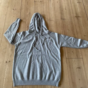 Grå merinoull hoodie  - Säljer en stilren grå merinoull hoodie med luva och dragsko. Tröjan har långa ärmar och ribbade muddar vid ärmslut och nederkant. Perfekt till jeans.