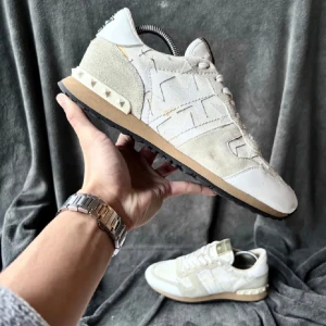 Valentino rockrunners  - Snygga Valentino sneakers i en kombination av beige mocka och vitt skinn. Skorna har en unik design med stjärnmönster och nitar på sulan. Perfekta för en stilren look.