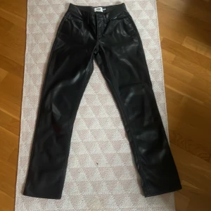 Svarta skinnbyxor - Snygga svarta skinnbyxor med låg midja och en stilren design. Byxorna har en rak passform och stängs med dragkedja och knapp framtill. Perfekta för en trendig look.