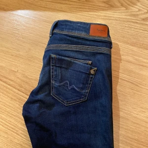 Blå jeans från Pepe Jeans - Snygga blå jeans från Pepe Jeans med klassisk femficksdesign och kontrasterande sömmar. Perfekta för en avslappnad stil. Märkesdetaljer på bakfickan och insidan av linningen. W 28, L 30. Midwaist, straight