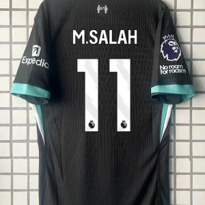 Svart fotbollströja med M. Salah 11 - Snygg svart fotbollströja med M. Salahs namn och nummer 11 på ryggen. Tröjan har korta ärmar med turkosa detaljer och Premier League-logga på ärmen. Perfekt för fans av Liverpool och Salah!
