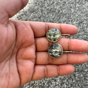 Örhängen med landskapsmotiv - Unika örhängen med vackert landskapsmotiv i runda hängen. De har en silverfärgad ram och krok för enkel användning. Perfekta för att ge en konstnärlig touch till din stil.