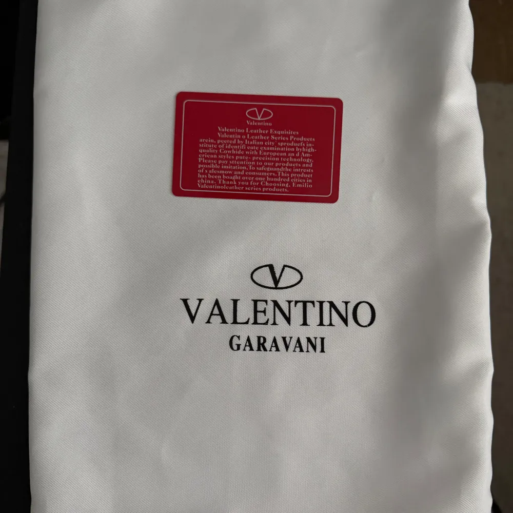 Vit dustbag från Valentino Garavani med logotypen tryckt i svart. Perfekt för att skydda dina exklusiva väskor eller accessoarer. Dustbagen har en rektangulär form och är tillverkad i ett mjukt material.. Asusteet.