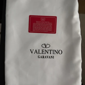 Vit dustbag från Valentino Garavani - Vit dustbag från Valentino Garavani med logotypen tryckt i svart. Perfekt för att skydda dina exklusiva väskor eller accessoarer. Dustbagen har en rektangulär form och är tillverkad i ett mjukt material.