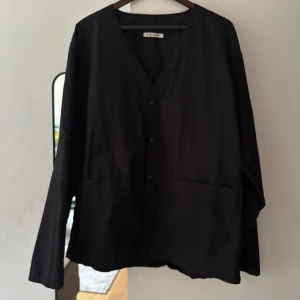 Svart overshirt från Our Legacy - Snygg svart overshirt från Our Legacy med knappar framtill. Den har en stilren design med långa ärmar och två praktiska fickor. Perfekt för en minimalistisk look.    Fitter Xl