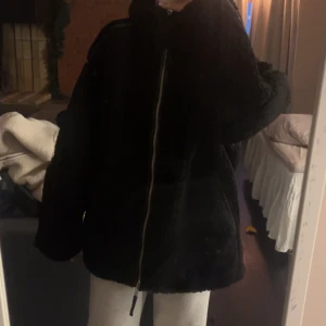 Svart teddyjacka med dragkedja - Mysig svart teddyjacka med dragkedja framtill. Perfekt för kyliga dagar med sin oversized passform och långa ärmar. Jackan har en enkel och stilren design som passar till många olika outfits.