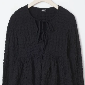 Svart långärmad blus från Gina Tricot - Snygg svart blus från Gina Tricot med lång ärm och knytning framtill. Perfekt för en stilren look. Blusen har en texturerad yta som ger en unik touch. Använd endast ett par fåtal gånger, inga defekter! Ordinarie pris 400kr