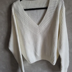 Vit stickad tröja från House Brand - Säljer en stilren vit stickad tröja från House Brand. Tröjan har en djup v-ringning och långa ärmar, perfekt för kyligare dagar. Den är mjuk och bekväm med ribbade detaljer vid hals och ärmslut.