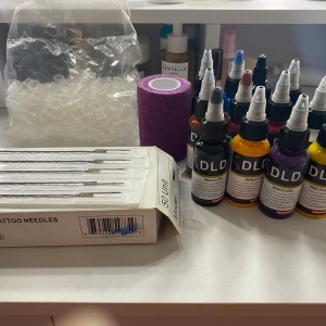DIY tatueringskit stick and poke  - 45st steriliserade engångsnålar. 14 st bläckflaskor från märket DLD i olika färger som svart, rött och vit. Även en stencil kräm. Det finns även en rulle lila bandage och en påse med plastkoppar för bläck. Perfekt för tatueringsentusiaster eller professionella tatuerare.