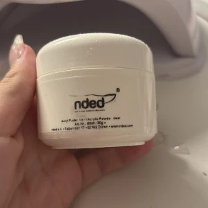 Acrylic Powder Clear 6000 från nded - Säljer en burk med klart akrylpulver från nded, perfekt för nagelförlängning och nageldesign. Produkten kommer i en praktisk vit burk med skruvlock och innehåller 30g. Märkt med säkerhetssymboler för korrekt hantering.