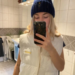 Vit och gul dunväst från Ganni - Säljer en snygg dunvästi både vit och gul färg. Den är vändbar. Västen har en dragkedja framtill och en broderad logga på bröstet. Perfekt till afterskin.