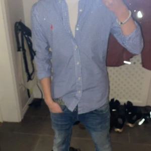 Blå och vit rutig skjorta från Polo Ralph Lauren - Snygg blå och vit rutig skjorta från Polo Ralph Lauren i slim fit. Skjortan har långa ärmar och knappar framtill. Perfekt för en stilren look.