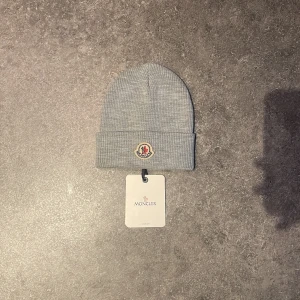 Grå Moncler mössa - Hej! Säljer denna snygga gråa  mössan från Moncler med broderad logotyp framtill. Perfekt för kyliga dagar och en stilren look. Pris 800 kr