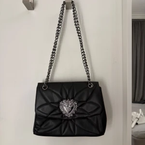 Liknande Dolce & Gabbana axelväska - Snygg svart axelväska i skinn från liknande Dolce & Gabbana med quiltad design och en iögonfallande hjärtformad detalj framtill. Kolla sista bilden för defekter 