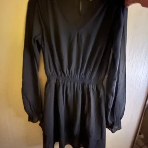 Svart klänning från Ullared  pris kan diskuteras helt ny alrdrig använd - Elegant svart klänning från Ullared med v-ringning och långa ärmar. Den har en elastisk midja som ger en smickrande passform. Perfekt för en stilren look.