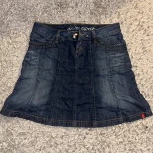 Jeanskjol från Esprit - Snygg jeanskjol från Esprit i klassisk blå denim. Kjolen har en kort längd och är försedd med två bakfickor med flätade detaljer. Perfekt för en avslappnad stil.