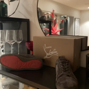 Christian Louboutin skor - Snygga grå sneakers i mocka från Christian Louboutin med den ikoniska röda sulan. Skorna har snörning och en stilren design som passar perfekt för en trendig look. Storleken är 41 men passar defensivt 42. ( köpt för 3499 säljer för 2199