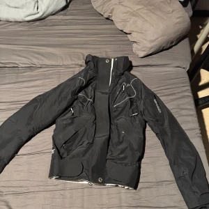 Svart peak performance skid jacka - Säljer en svart jacka från Peak performance med dragkedja och flera fickor. Jackan har en sportig design med vita detaljer och är perfekt för kyligare väder ock skid backen. Den är i storlek S men sitter som XS