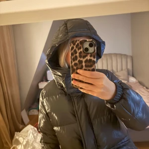 Svart pufferjacka från Colmar - Säljer en svart pufferjacka från Colmar. Jackan har en hög krage och en stor huva för extra värme. Den är utrustad med dragkedja och har en glansig yta som ger en stilren look. Perfekt för kyliga dagar! 