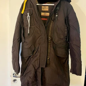 Brun vinterjacka från Parajumpers - Säljer en brun vinterjacka från Parajumpers, Masterpiece Series. Jackan har en slim fit passform och är utrustad med flera praktiska fickor och en dragkedja. Den har en gul detalj vid kragen och är perfekt för kalla vinterdagar.