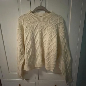 Stickad tröja från SRN HLT - Mysig vanilj färgad stickad tröja från SRN HLT med klassiskt flätmönster. Perfekt nu för kyliga vinter dagar med sin sköna design. Tröjan har långa ärmar och en ribbad krage som ger en stilren look. Köpt på Ullared. ✨🫧