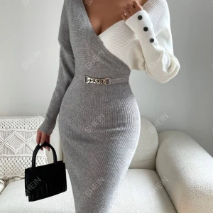 Grå och vit omlottklänning från SHEIN - Snygg grå och vit omlottklänning från SHEIN med en unik design. Klänningen har en offshoulder-stil och är ribbad med en dekorativ metallkedja i midjan. Ena ärmen är lång och grå medan den andra är vit med svarta knappar.