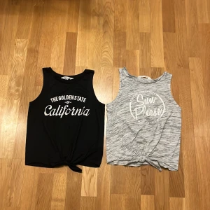 Två ärmlösa toppar med tryck - Säljer två snygga ärmlösa toppar. En svart topp med texten 'The Golden State of California' och en gråmelerad topp med texten 'Sun Please'. Båda topparna har en knutdetalj framtill. Perfekta för en avslappnad stil!