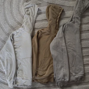 Tre hoodies i olika färger - Säljer tre bekväma hoodies i färgerna beige, brun och grå. Perfekta för en avslappnad stil med klassisk design och känguruficka framtill. Huvtröjorna har långa ärmar och är gjorda i mjukt material. Den gråa har ett pyttelitet hål men det lagas lätt med nål och tråd. Annars är fem i gott skick. Storlek; 146/158. 75:-/st eller alla 3 för 200:-