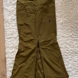 Olivgrön kjol från GeckoWear - Snygg olivgrön långkjol med dragkedja fram och bak samt fickor framtill. Kjolen har bara varit med om en dansnatt så den är i perfekt skick.  Justerbara snören i midjan. Storlek M/L. Unik look. Kjolen är inköpt på GeckoWear i Malmö 🦎 