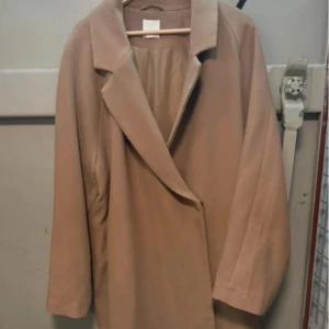 Beige kappa från H&M - Snygg beige kappa från H&M i en klassisk design. Perfekt för höst och vår med sin stilrena look och långa ärmar. Kappan har en elegant krage och är tillverkad i ett mjukt material. Pris kan diskuteras