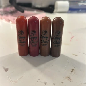 Lippy Chic läppstift i fyra färger - Fyra olika nyanser av Lippy Chic läppstift från W7. Färgerna inkluderar en varm orange, en djup röd, en mjuk brun och en mörkare brun. Perfekta för att variera din look med olika färgtoner.