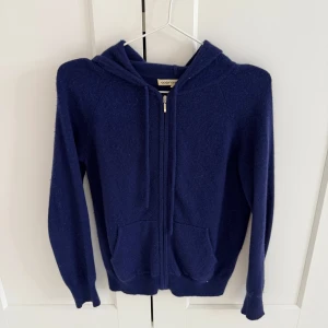 Mörkblå hoodie från Cozy Cashmere - Säljer en supermjuk och bekväm mörkblå hoodie från Cozy Cashmere. Den har en dragkedja framtill och en praktisk huva. Perfekt för kyliga dagar när du vill känna dig både stilren och avslappnad.