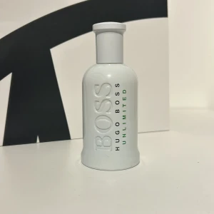 Hugo Boss Unlimited Parfym - Säljer en stilren och fräsch parfymflaska från Hugo Boss. Flaskan är vit med texten 'BOSS' i relief och 'HUGO BOSS UNLIMITED' i grönt och svart. Perfekt för den som vill ha en modern och energisk doft. Det är cirka halva parfymen kvar,