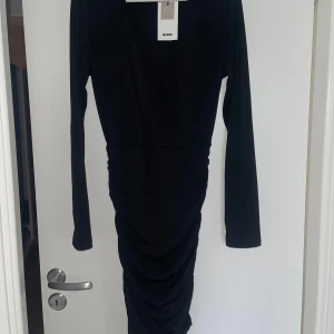 Svart långärmad klänning - Elegant svart klänning med långa ärmar och en åtsittande passform. Klänningen har en stilren design och är perfekt för en kväll ute. Materialet är mjukt och bekvämt. Knappen måste sys till, Nypris 499kr